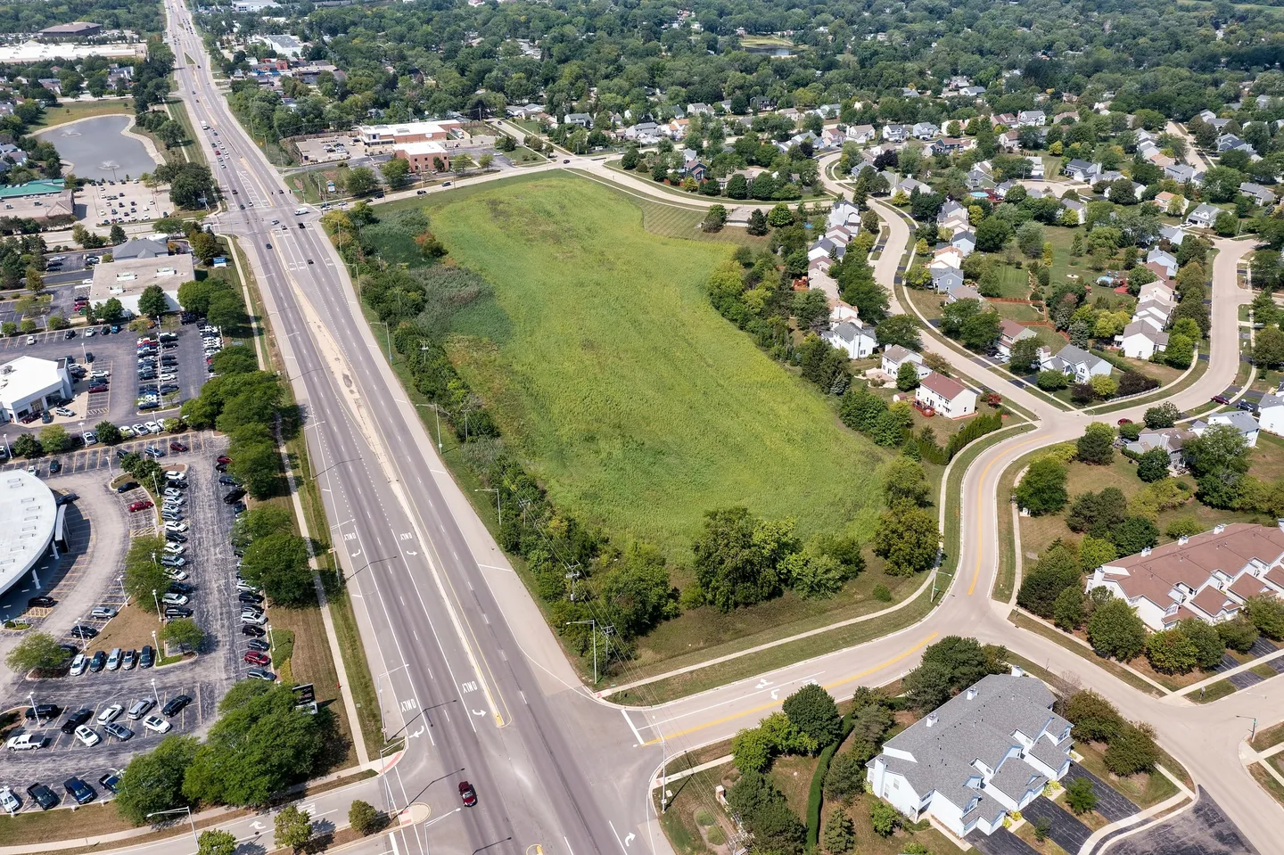 An aerial view of a green field with cars driving on the road.